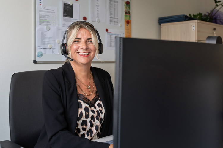 Mitarbeiterin im Forderungsmanagement an ihrem Arbeitsplatz. Sie lächelt freundlich in die Kamera.