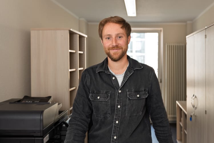 Ein Mitarbeiter der Mietkalkulation im Kopierraum blickt freundlich in die Kamera. 