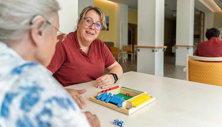 Eine Mitarbeiterin der Tagespflege spielt mit einer Besucherin ein Tischspiel. 