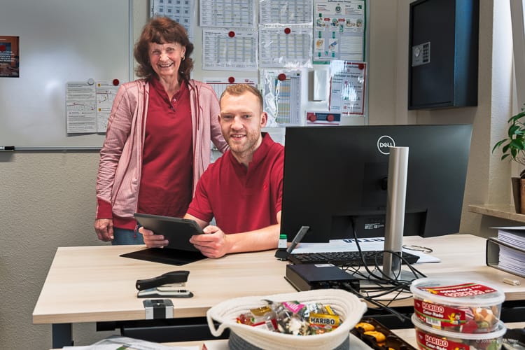 Zwei Pflegekräfte im Büro blicken freundlich in die Kamera.