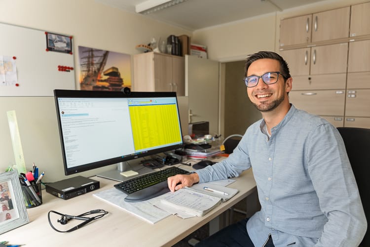 Ein Verwalter von Gewerbeimmobilien sitzt an seinem Arbeitsplatz und wendet sich dem Betrachter freundlich zu. 