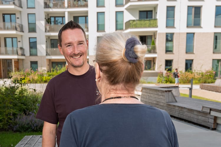 Ein Vermieter der WIRO im Gespräch mit einer Mieterin. Er blickt über deren Schulter freundlich in die Kamera. 