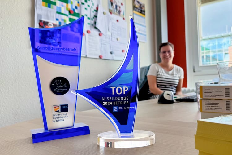 Nahaufnahme von zwei blauen Acryl-Auszeichnungen der IHK zu Rostock mit der Aufschrift „TOP Ausbildungsbetrieb“.