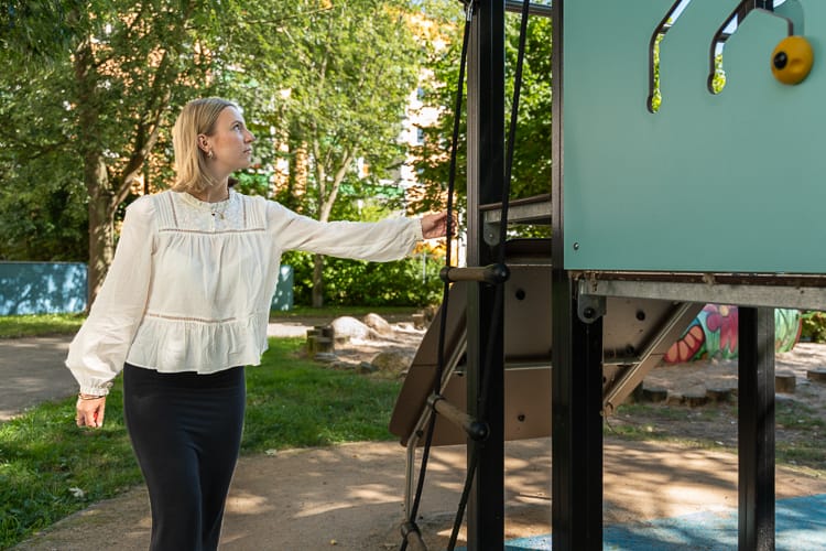 Eine WIRO-Auszubildende in heller Bluse und dunklem Rock inspiziert die Verkehrssicherheit eines Spielplatzgeräts.