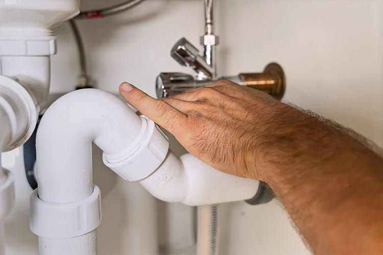 Nahaufnahme der Hand eines Installateurs der in einem Bad an einem weißen Siphon unter der Spüle arbeitet