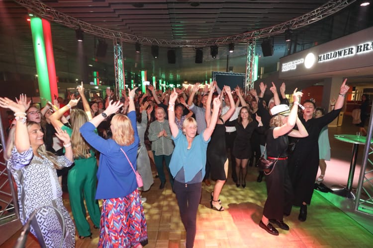 Zahlreiche WIRO-Mitarbeiter feiern ausgelassen auf einer Betriebsfeier. Die tanzenden Menschen strecken die Arme in die Höhe, während bunte Lichter die Tanzfläche erhellen.