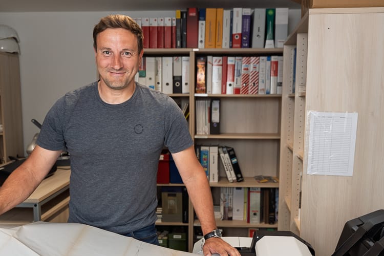 Drei junge WIRO-Mitarbeiter stehen lächelnd vor dem KundenCenter Groß Klein. Der Mann trägt eine rote Latzhose, die Frauen tragen elegante Business-Kleidung.