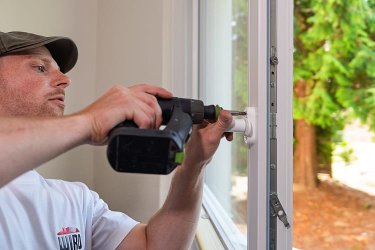 Ein Tischler montiert mit einem Akkuschrauber einen Fensterbeschlag.