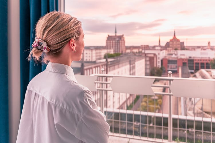 Eine Frau blickt aus einem oberen Stock über Rostock. Es ist morgendliche Stimmung.