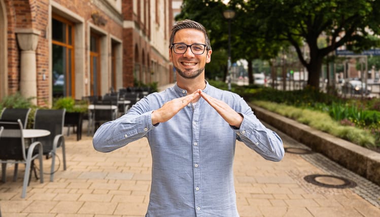 Ein Verwalter für Gewerbeimmobilien blickt freundlich in die Kamera und zeigt mit seinen Händen eine Dachgeste. 