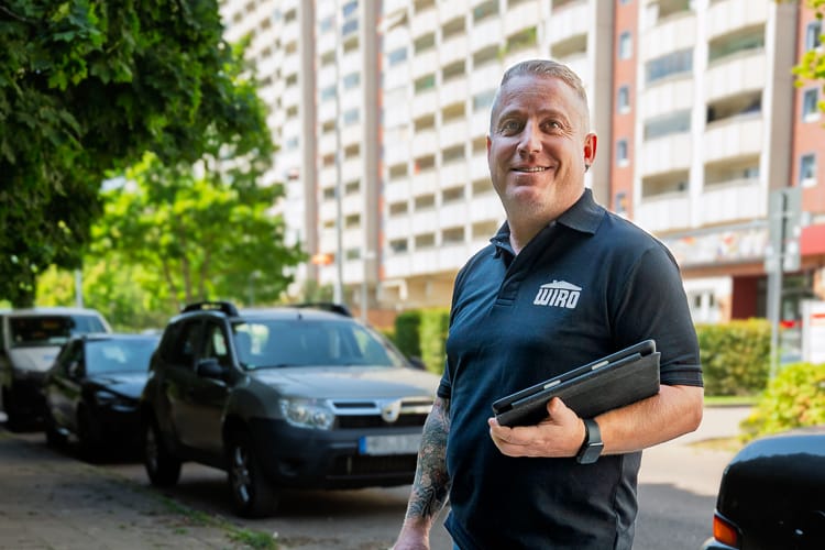 Ein Wohnungsverwalter der WIRO steht vor einer großen Wohnanlage und blickt freundlich in die Kamera.
