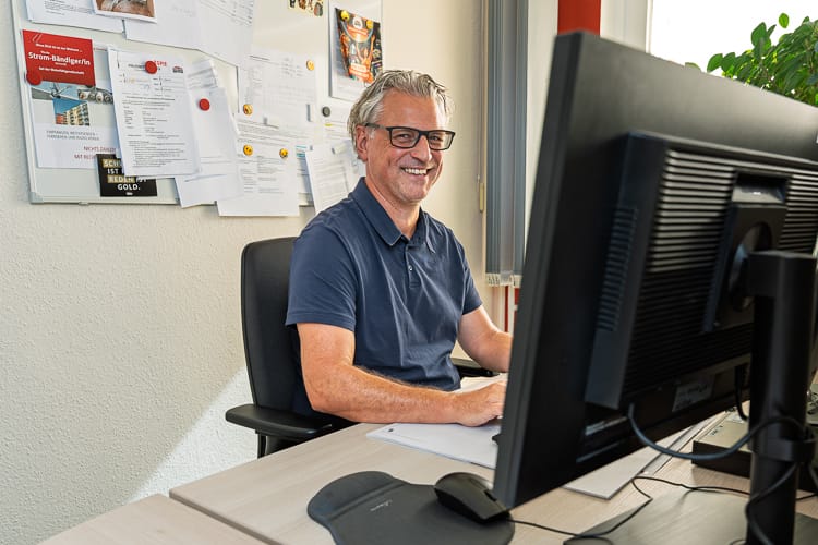 Drei junge WIRO-Mitarbeiter stehen lächelnd vor dem KundenCenter Groß Klein. Der Mann trägt eine rote Latzhose, die Frauen tragen elegante Business-Kleidung.