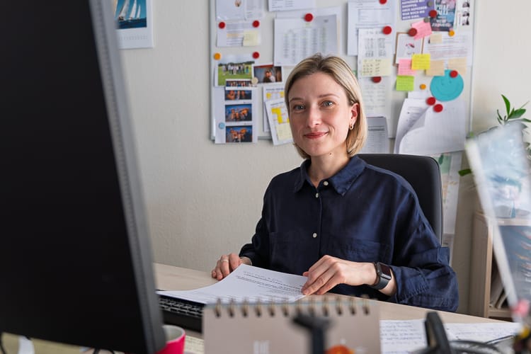 Eine Mitarbeiterin der WIRO sitzt an ihrem Schreibtisch und blickt freundlich in die Kamera.